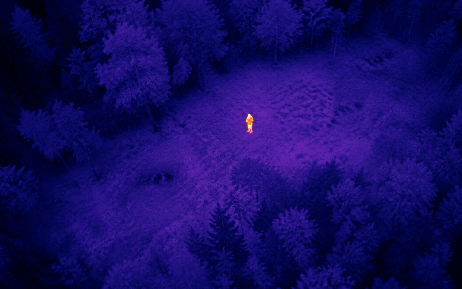 Thermal drone view showing a person in a wooded clearing during search and rescue support